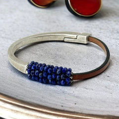 Artisan bracelet featuring a silver-tone half cuff and brown leather band, hand-stitched with faceted lapis beads and a signature gold accent; Martell Studio design, size 6 with magnetic clasp.