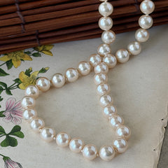 A vintage Marvella cream faux pearl necklace with hand‑knotted pearls and a gold‑tone slide clasp, displayed  with soft natural light highlighting the luster of the pearls.