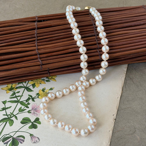 A vintage Marvella cream faux pearl necklace with hand‑knotted pearls and a gold‑tone slide clasp, displayed  with soft natural light highlighting the luster of the pearls.