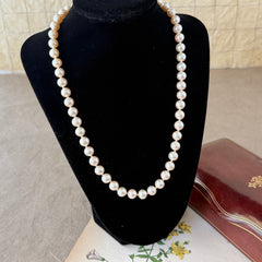 A vintage Marvella cream faux pearl necklace with hand‑knotted pearls and a gold‑tone slide clasp, displayed  with soft natural light highlighting the luster of the pearls.