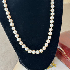 A vintage Marvella cream faux pearl necklace with hand‑knotted pearls and a gold‑tone slide clasp, displayed  with soft natural light highlighting the luster of the pearls.