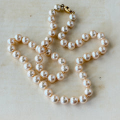 A vintage Marvella cream faux pearl necklace with hand‑knotted pearls and a gold‑tone slide clasp, displayed  with soft natural light highlighting the luster of the pearls.
