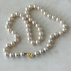 A vintage Marvella cream faux pearl necklace with hand‑knotted pearls and a gold‑tone slide clasp, displayed  with soft natural light highlighting the luster of the pearls.