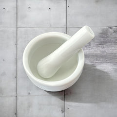Elegant white porcelain mortar and pestle with glazed exterior and raw interior, designed for tabletop spice grinding and culinary rituals.