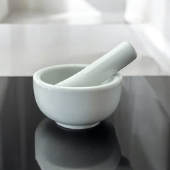 Elegant white porcelain mortar and pestle with glazed exterior and raw interior, designed for tabletop spice grinding and culinary rituals.