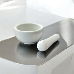 Elegant white porcelain mortar and pestle with glazed exterior and raw interior, designed for tabletop spice grinding and culinary rituals.