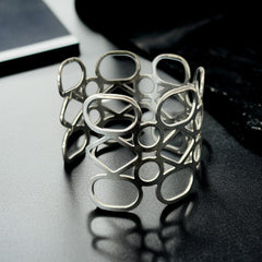 Silver tone cuff bracelet with polished openwork design featuring interconnected ovals, circles, and diamond shapes; modern, unsigned piece with a sleek finish and subtle surface wear.