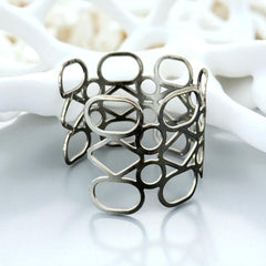 Silver tone cuff bracelet with polished openwork design featuring interconnected ovals, circles, and diamond shapes; modern, unsigned piece with a sleek finish and subtle surface wear.