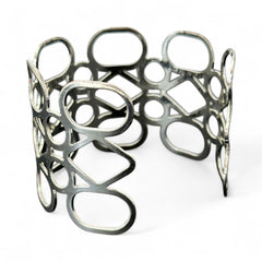 Silver tone cuff bracelet with polished openwork design featuring interconnected ovals, circles, and diamond shapes; modern, unsigned piece with a sleek finish and subtle surface wear.