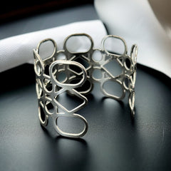 Silver tone cuff bracelet with polished openwork design featuring interconnected ovals, circles, and diamond shapes; modern, unsigned piece with a sleek finish and subtle surface wear.