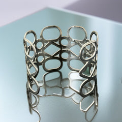 Silver tone cuff bracelet with polished openwork design featuring interconnected ovals, circles, and diamond shapes; modern, unsigned piece with a sleek finish and subtle surface wear.