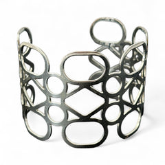 Silver tone cuff bracelet with polished openwork design featuring interconnected ovals, circles, and diamond shapes; modern, unsigned piece with a sleek finish and subtle surface wear.