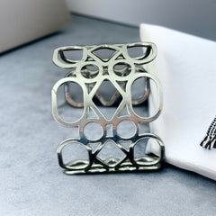 Silver tone cuff bracelet with polished openwork design featuring interconnected ovals, circles, and diamond shapes; modern, unsigned piece with a sleek finish and subtle surface wear.