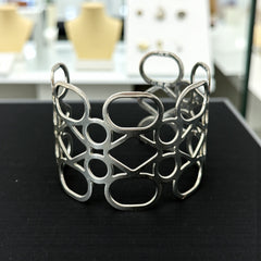 Silver tone cuff bracelet with polished openwork design featuring interconnected ovals, circles, and diamond shapes; modern, unsigned piece with a sleek finish and subtle surface wear.