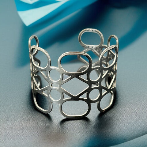 Silver tone cuff bracelet with polished openwork design featuring interconnected ovals, circles, and diamond shapes; modern, unsigned piece with a sleek finish and subtle surface wear.