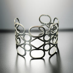 Silver tone cuff bracelet with polished openwork design featuring interconnected ovals, circles, and diamond shapes; modern, unsigned piece with a sleek finish and subtle surface wear.