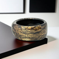 Glossy black and gold Lucite bangle with a freeform silhouette and layered, crackled texture; unsigned and sculptural.