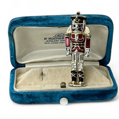 Vintage Monet nutcracker brooch with red and clear rhinestones, black and red enamel, and light gold tone finish, signed on back, holiday-themed costume jewelry in excellent condition
