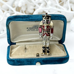 Vintage Monet nutcracker brooch with red and clear rhinestones, black and red enamel, and light gold tone finish, signed on back, holiday-themed costume jewelry in excellent condition