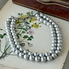 Vintage Monet brushed silver tone two‑strand bead necklace displayed on a black velvet bust and vintage botanical background.