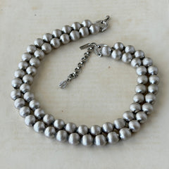 Vintage Monet brushed silver tone two‑strand bead necklace displayed on a black velvet bust and vintage botanical background.