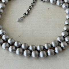 Vintage Monet brushed silver tone two‑strand bead necklace displayed on a black velvet bust and vintage botanical background.