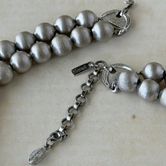 Vintage Monet brushed silver tone two‑strand bead necklace displayed on a black velvet bust and vintage botanical background.