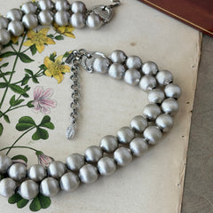Vintage Monet brushed silver tone two‑strand bead necklace displayed on a black velvet bust and vintage botanical background.