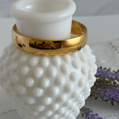 Vintage Monet gold‑tone bangle bracelet with a smooth polished finish displayed on an ornate stand.
