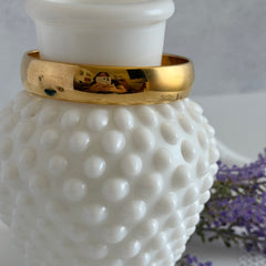 Vintage Monet gold‑tone bangle bracelet with a smooth polished finish displayed on an ornate stand.