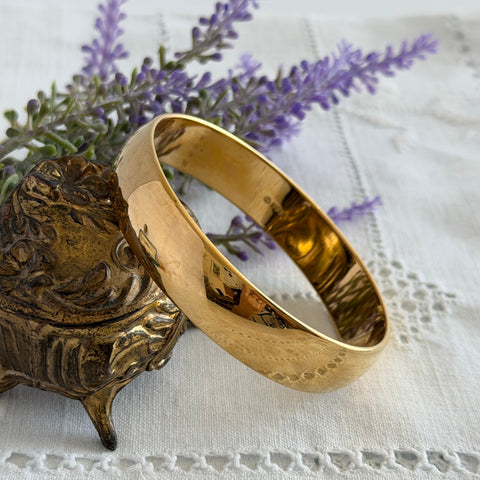 Vintage Monet gold‑tone bangle bracelet with a smooth polished finish displayed on an ornate stand.