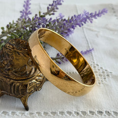 Vintage Monet gold‑tone bangle bracelet with a smooth polished finish displayed on an ornate stand.