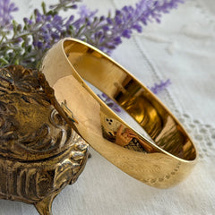 Vintage Monet gold‑tone bangle bracelet with a smooth polished finish displayed on an ornate stand.
