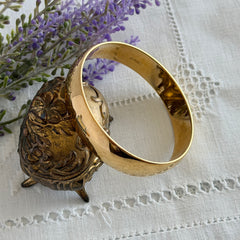 Vintage Monet gold‑tone bangle bracelet with a smooth polished finish displayed on an ornate stand.
