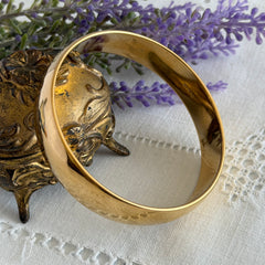 Vintage Monet gold‑tone bangle bracelet with a smooth polished finish displayed on an ornate stand.
