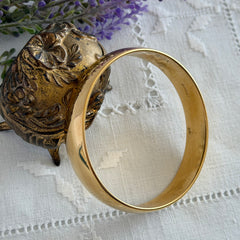 Vintage Monet gold‑tone bangle bracelet with a smooth polished finish displayed on an ornate stand.