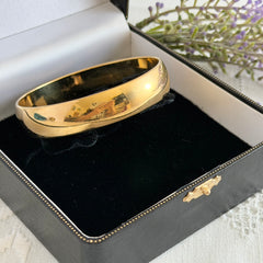Vintage Monet gold‑tone bangle bracelet with a smooth polished finish displayed on an ornate stand.