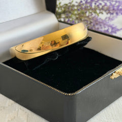 Vintage Monet gold‑tone bangle bracelet with a smooth polished finish displayed on an ornate stand.
