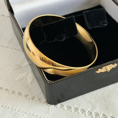 Vintage Monet gold‑tone bangle bracelet with a smooth polished finish displayed on an ornate stand.