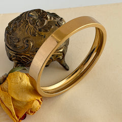 Vintage Monet gold‑tone minimalist bangle bracelet with a smooth polished finish, shown in close‑up on a neutral background.
