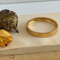 Vintage Monet gold‑tone minimalist bangle bracelet with a smooth polished finish, shown in close‑up on a neutral background.