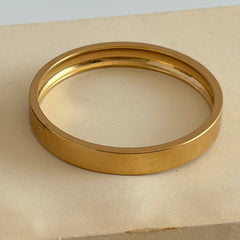 Vintage Monet gold‑tone minimalist bangle bracelet with a smooth polished finish, shown in close‑up on a neutral background.