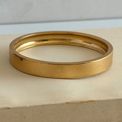 Vintage Monet gold‑tone minimalist bangle bracelet with a smooth polished finish, shown in close‑up on a neutral background.