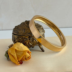 Vintage Monet gold‑tone minimalist bangle bracelet with a smooth polished finish, shown in close‑up on a neutral background.