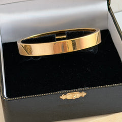 Vintage Monet gold‑tone minimalist bangle bracelet with a smooth polished finish, shown in close‑up on a neutral background.
