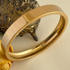 Vintage Monet gold‑tone minimalist bangle bracelet with a smooth polished finish, shown in close‑up on a neutral background.