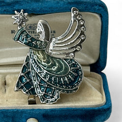Vintage Monet angel brooch in silver tone metal with teal and light green enamel robe, clear rhinestone wings, and raised star detail; signed Monet on back.