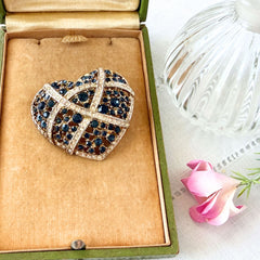 Vintage heart brooch with Montana sapphire and clear rhinestones in silver‑tone metal with gold wash, displayed on lace with a green book and pink flower
