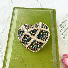 Vintage heart brooch with Montana sapphire and clear rhinestones in silver‑tone metal with gold wash, displayed on lace with a green book and pink flower