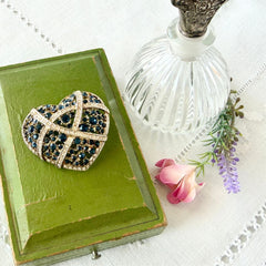 Vintage heart brooch with Montana sapphire and clear rhinestones in silver‑tone metal with gold wash, displayed on lace with a green book and pink flower